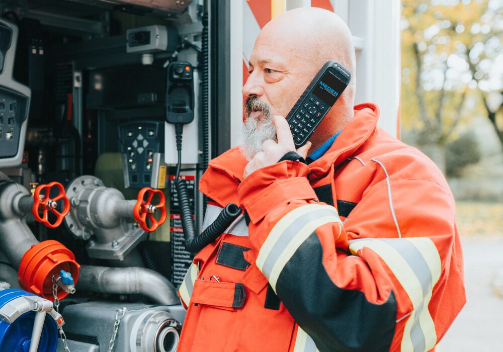 Feuerwehrmann nutzt Funkgerät mit LARDIS-Technologie zur Koordination direkt am Einsatzfahrzeug, ausgestattet mit modernster Technik für effektive Kommunikation.